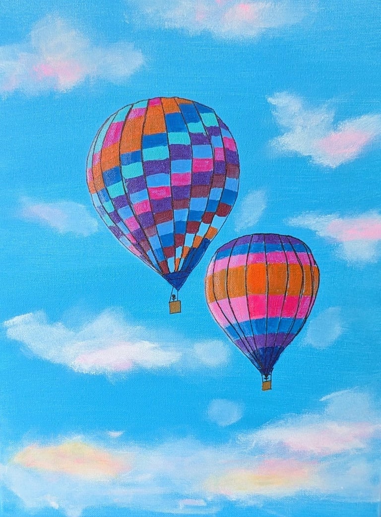 Two colorful hot air balloons floating in a bright blue sky with white and pink clouds