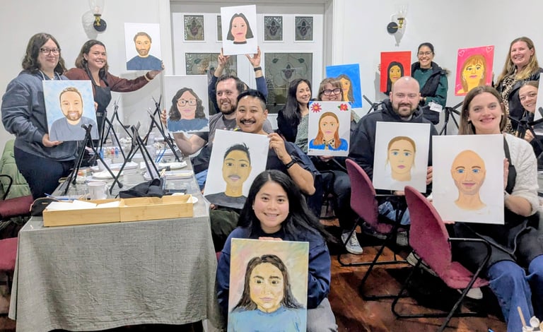 Group of people holding colorful portrait drawings they created, smiling at camera in an art class or workshop setting