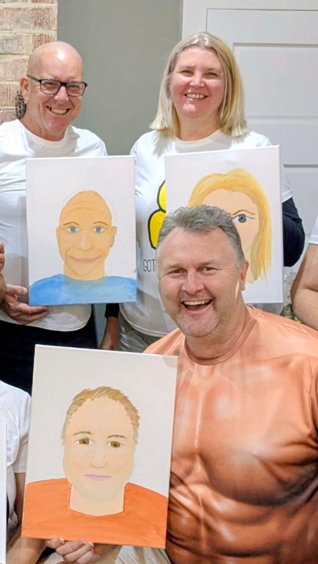 Three smiling people holding hand-drawn portrait paintings of themselves in what appears to be an art class or workshop setting